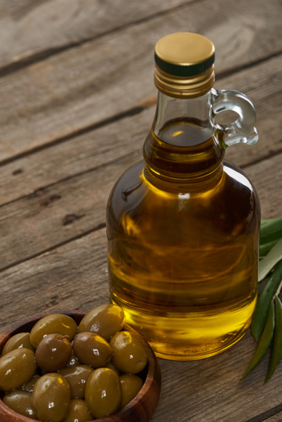 oil bottle, bowl of olives and olive tree leaves on wooden surface  - Foto, afbeelding