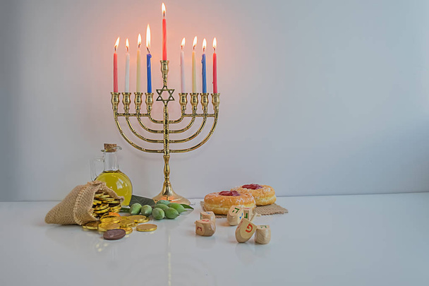 Fiesta judía de Hanukkah celebración con menorah (candelabros tradicionales), dreidels de madera (spinning top), donut, aceite de oliva y monedas de chocolate en la mesa blanca. mesa. cuadro
. - Foto, Imagen