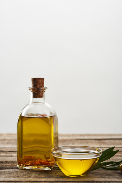 bottle and glass bowl of olive oil, olive tree leaves and olives on wooden surface - Foto, Imagen