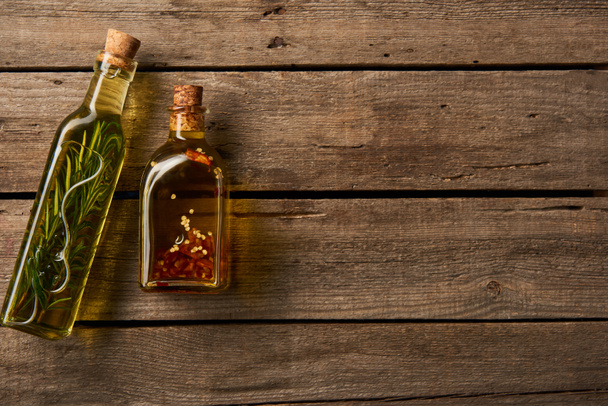 top view of bottles with oil flavored with rosemary and spices on wooden background - Φωτογραφία, εικόνα