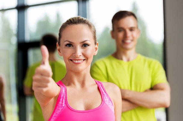 smiling man and woman showing thumbs up in gym - Photo, image