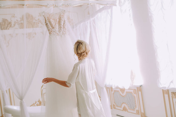 bride is touching bridal wedding dress in a luxury bedroom above the bed in the interior - Foto, Bild