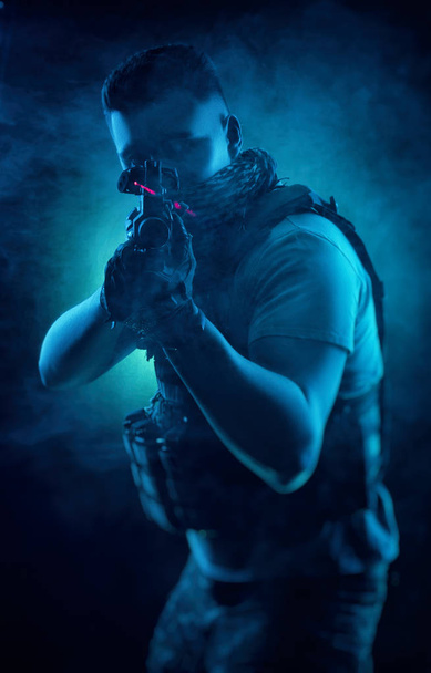 o homem de roupas especiais militares posando com uma arma em suas mãos em um fundo escuro na névoa
 - Foto, Imagem