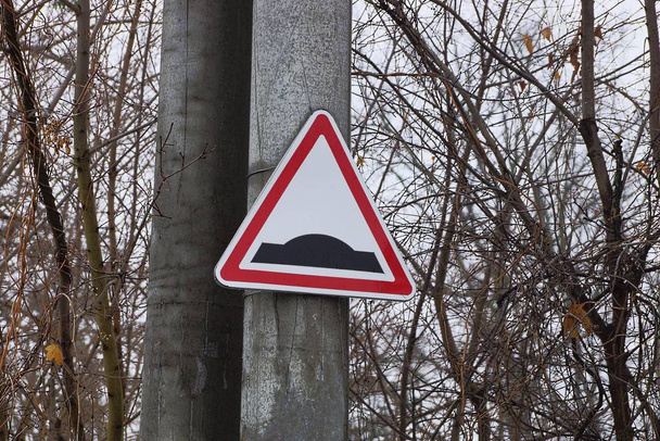 triangular road sign speed bump on a concrete pillar among tree branches - Photo, Image