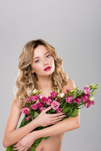 nude beautiful blonde woman posing with spring Eustoma flowers bouquet isolated on grey - 写真・画像