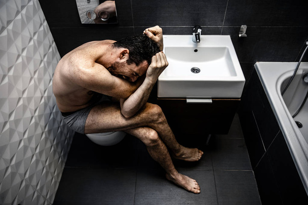 Naked man sitting in the old city toilet. Person feels terrible emotional pain and helplessness. The addict feels bad. - Photo, Image