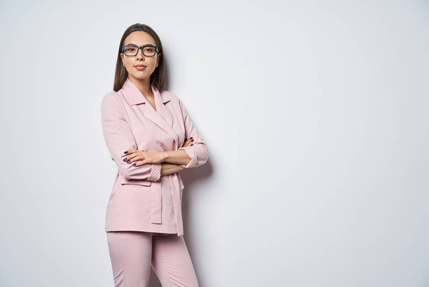 Confident business woman wearing pink suit standing by white wall with folded hands - Φωτογραφία, εικόνα
