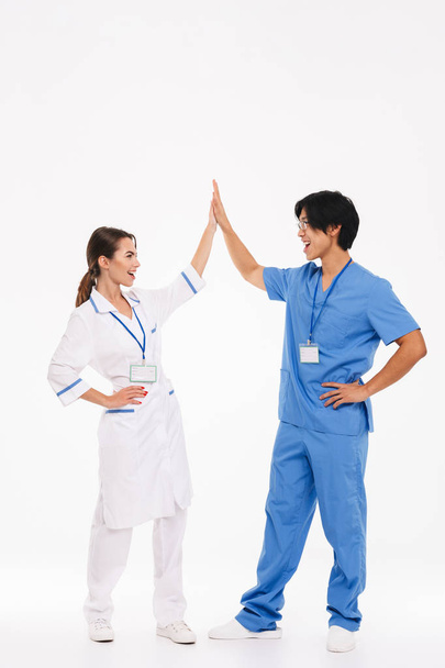 Feliz pareja de médicos vistiendo uniforme de pie aislado sobre fondo blanco, dando alta cinco
 - Foto, imagen