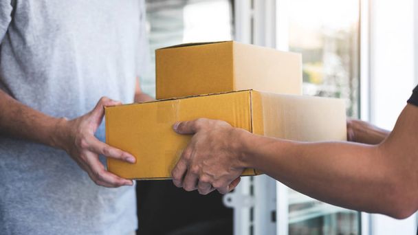Почтальон, дающий посылку коробку получателю, молодой владелец, принимающий пакет картонных коробок от почтовой доставки, Home courier и службы доставки концепции разума
. - Фото, изображение