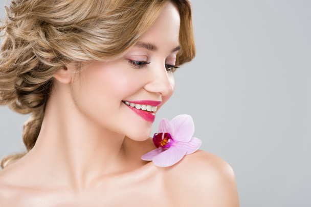 young smiling naked woman with purple orchid on shoulder isolated on grey - Photo, Image