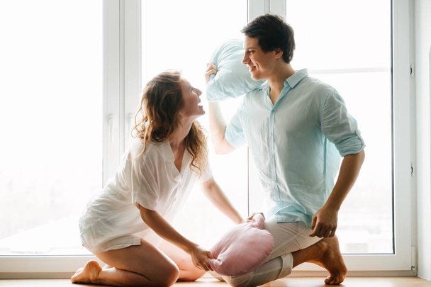 Couple girl and guy play with pillows near window. - Photo, image