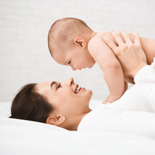 Mother with baby on bed having good time - Foto, afbeelding