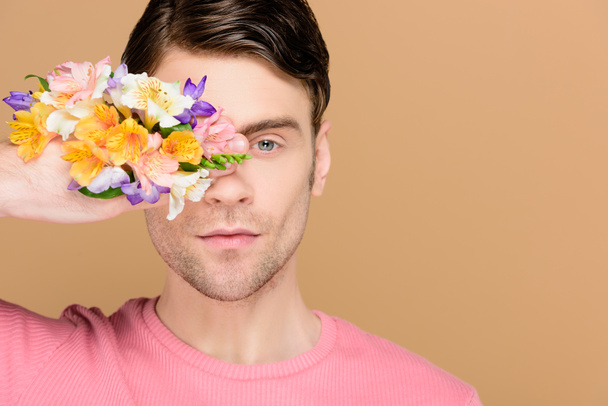 uomo sicuro di sé che copre un occhio con i fiori a portata di mano isolato su beige
 - Foto, immagini