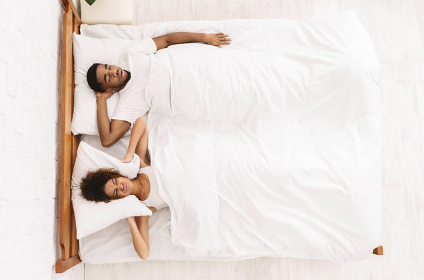 Uni-ongelmia. Afrikkalainen-amerikkalainen nainen sulkemalla korvansa tyynyllä, piilossa ärsyttävää kuorsaus miehensä, ylhäältä näkymä vapaata tilaa
 - Valokuva, kuva