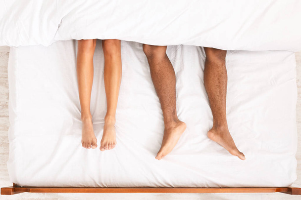 Male and female legs under duvet lying on bed - Fotó, kép