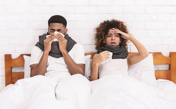 Sick african-american couple blowing noses in bed - Fotó, kép