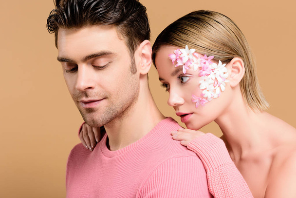 attractive woman with flowers on face looking at man isolated on beige  - Photo, Image