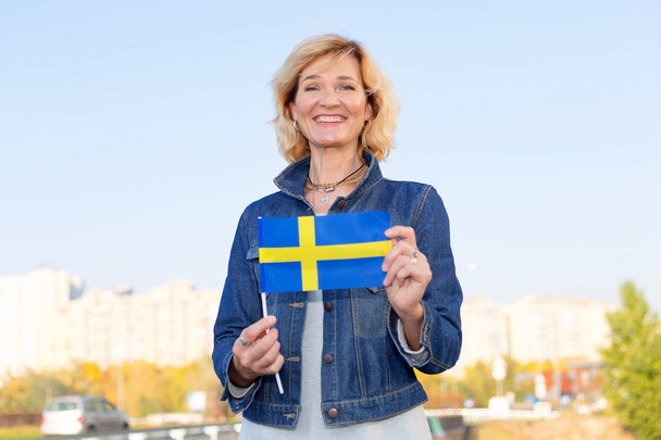 Mature woman with the flag of Sweden against the background of the city and the blue sky. - Foto, Imagem
