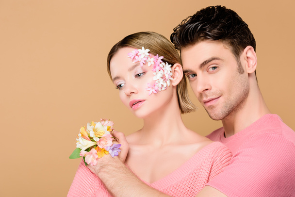 handsome boyfriend hugging girlfriend with flowers on face isolated on beige  - 写真・画像