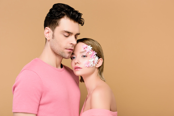 handsome man standing with beautiful woman with flowers on face isolated on beige  - Fotografie, Obrázek