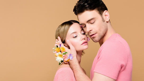 handsome man with alstroemeria flowers on hand touching face of attractive girlfriend isolated on beige  - Photo, image