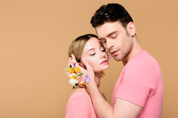 tender man with alstroemeria flowers on hand touching face of attractive girlfriend isolated on beige  - Fotó, kép