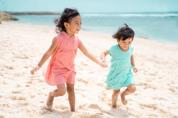 two little girl hold hand when walking on white sand seashore - Fotó, kép