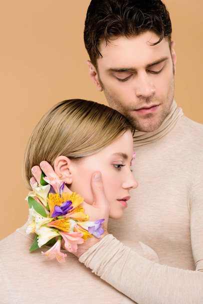 na straně řízení muž s květy kosatců dotýkání tváře krásné přítelkyně izolované na béžové  - Fotografie, Obrázek