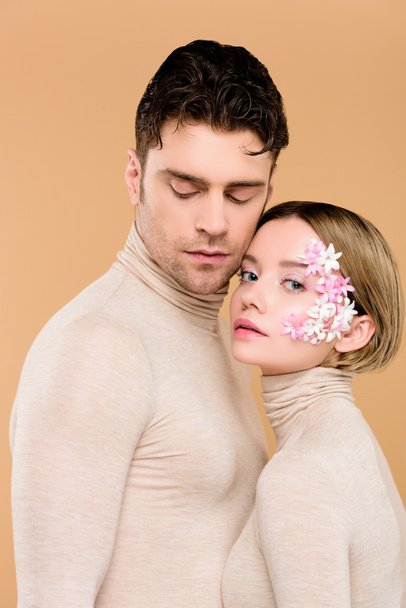 tender woman with flowers on face standing with handsome man isolated on beige  - Foto, afbeelding