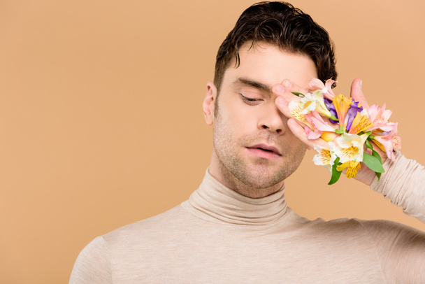 tenero uomo con fiori di alstroemeria a portata di mano che copre un occhio isolato sul beige
  - Foto, immagini