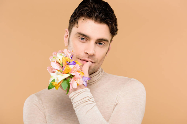 άνθρωπος με Αλστρομέριες λουλούδια στο χέρι αγγίζει τα χείλη που απομονώνονται σε μπεζ  - Φωτογραφία, εικόνα