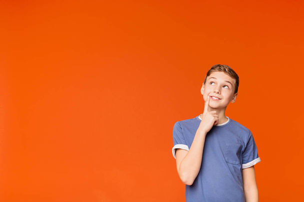 Tricky boy thinking about some prank on orange background - Foto, Imagem
