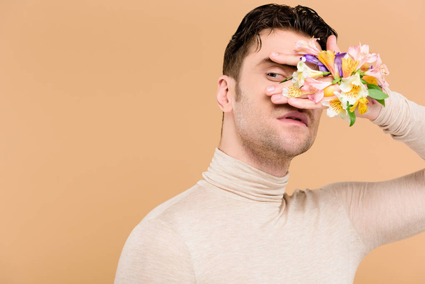handsome man with alstroemeria flowers on hand covering face isolated on beige  - Fotoğraf, Görsel