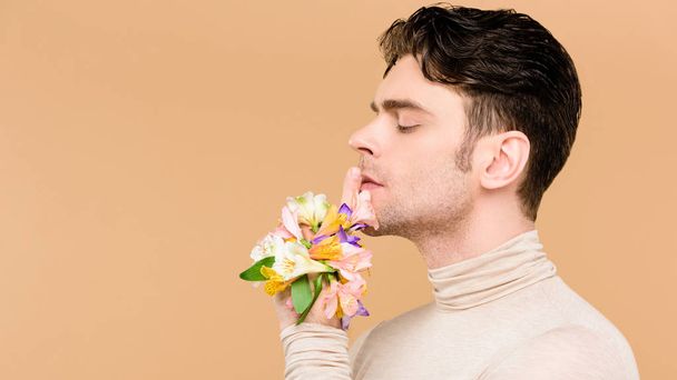 άποψη πλευρά των όμορφος άντρας με λουλούδια Αλστρομέριες αφενός δείχνει σημάδι hush απομονώνονται σε μπεζ  - Φωτογραφία, εικόνα