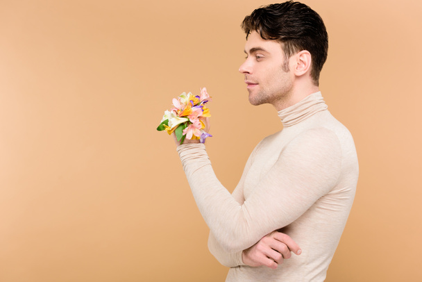 zamyślony człowiek z alstroemeria kwiaty na ręka stojący na beżowym tle  - Zdjęcie, obraz