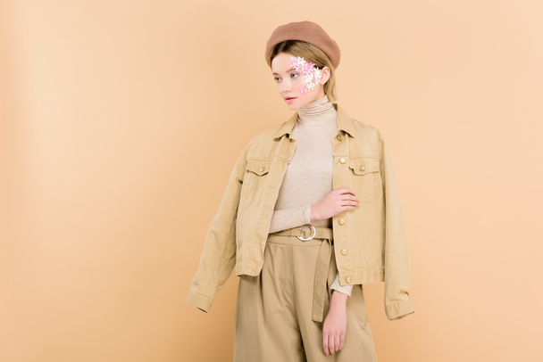 attractive woman with flowers on face wearing beret and standing isolated on beige  - Foto, afbeelding