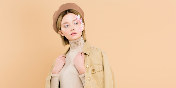 beautiful woman with flowers on face wearing beret and standing isolated on beige  - Photo, Image