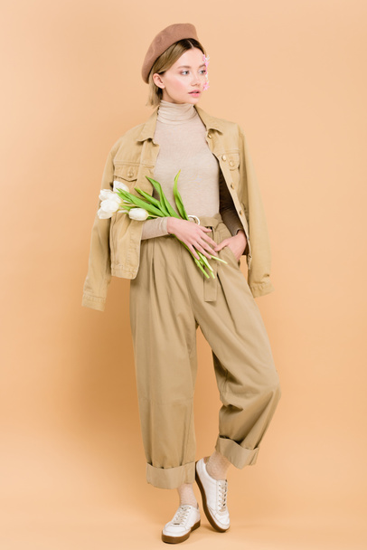 trendy woman wearing beret and holding bouquet isolated on beige  - Foto, immagini