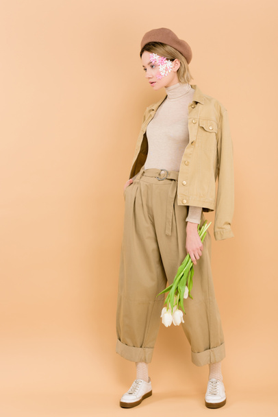 stylish woman in beret holding bouquet of flowers isolated on beige  - Photo, image