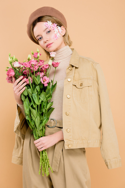 mulher na moda com flores no rosto segurando buquê isolado no bege
  - Foto, Imagem