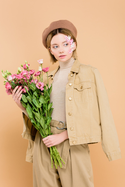 stylish woman with flowers on face holding bouquet isolated on beige  - Photo, Image