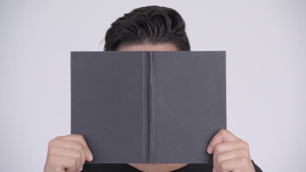 Face of young multi-ethnic nerd man covering face with book - Imágenes, Vídeo