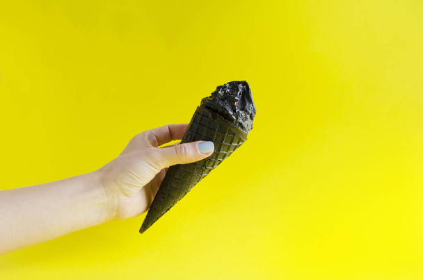 Woman proposing black ice cream against yellow background.Concept of atypical summer vacation.Copy space for your text - Photo, Image