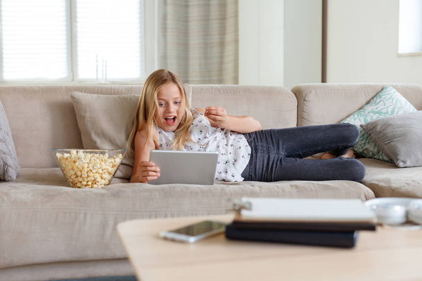 Excited girl lying down on sofa at home and watching a digital tablet.  - Fotoğraf, Görsel