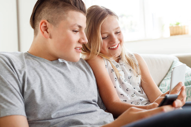 Brother and sister sitting on sofa in living room and using smart phones. - Fotó, kép