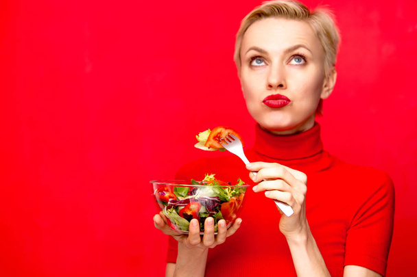 Beautiful woman eating salad wearing red dress and red lisptick over red background. Holiday, valentine day party concept - Foto, immagini