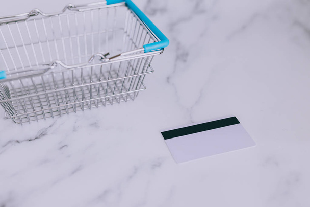 payment card on marble desk next to empty shopping basket, concept of budgeting for your expenses - Foto, Imagem