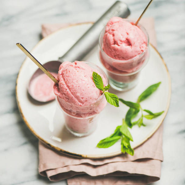 Healthy low calorie summer dessert. Homemade strawberry yogurt ice cream with fresh mint in glasses over light grey marble table background, square crop. Clean eating, dieting food concept - Photo, image