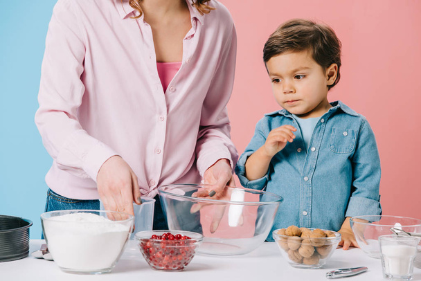 Netter kleiner Junge mit Mutter beim Vorbereiten von Zutaten zum Backen auf zweifarbigem Hintergrund - Foto, Bild