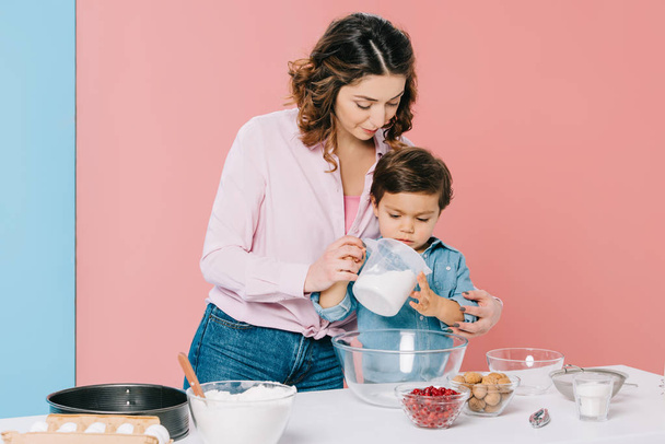 little boy attentively looking at measuring cup in mothers hands on bicolor background - Photo, Image